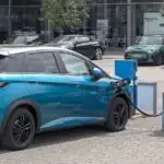 Turkusowy BYD Dolphin podłączony do stacji ładowania na parkingu