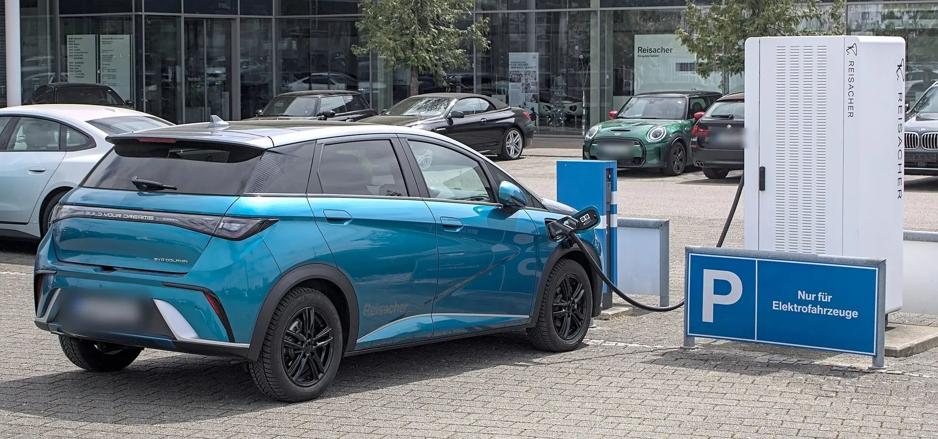 Turkusowy BYD Dolphin podłączony do stacji ładowania na parkingu