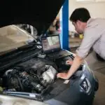 Mechanik pochylony nad silnikiem z laptopem diagnostycznym